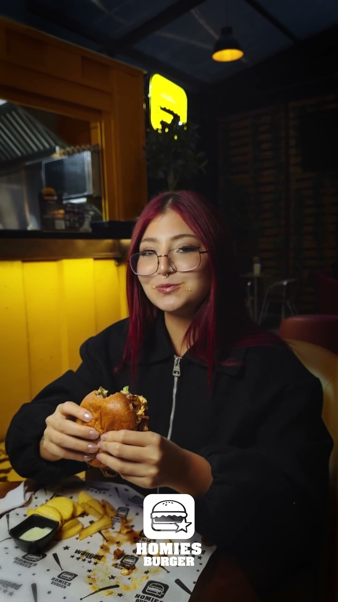 Sentada a la mesa de una hamburguesería, con la hamburguesa en las manos